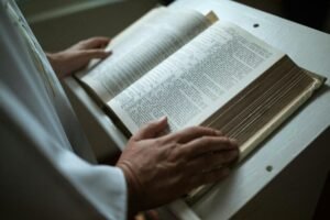 A person in white garment holds an open religious scripture, focusing on hands and text.